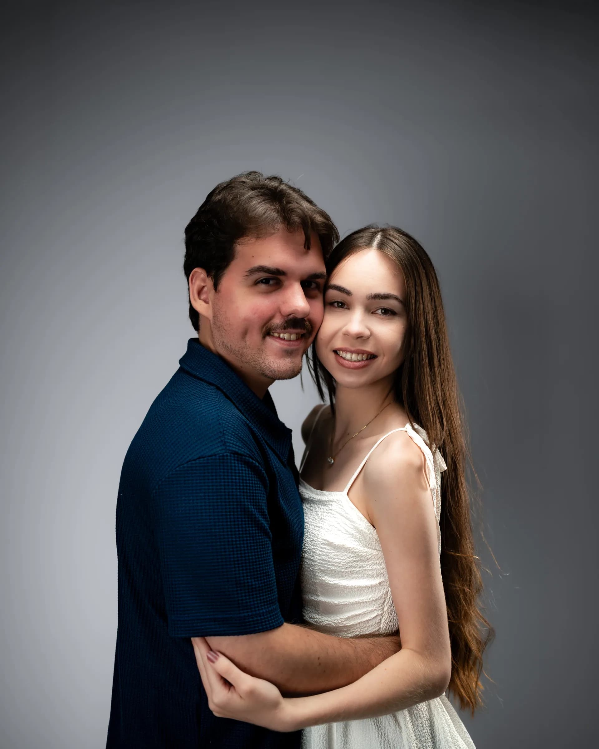 Casal abraçado de lado, os dois sorrindo para a câmera