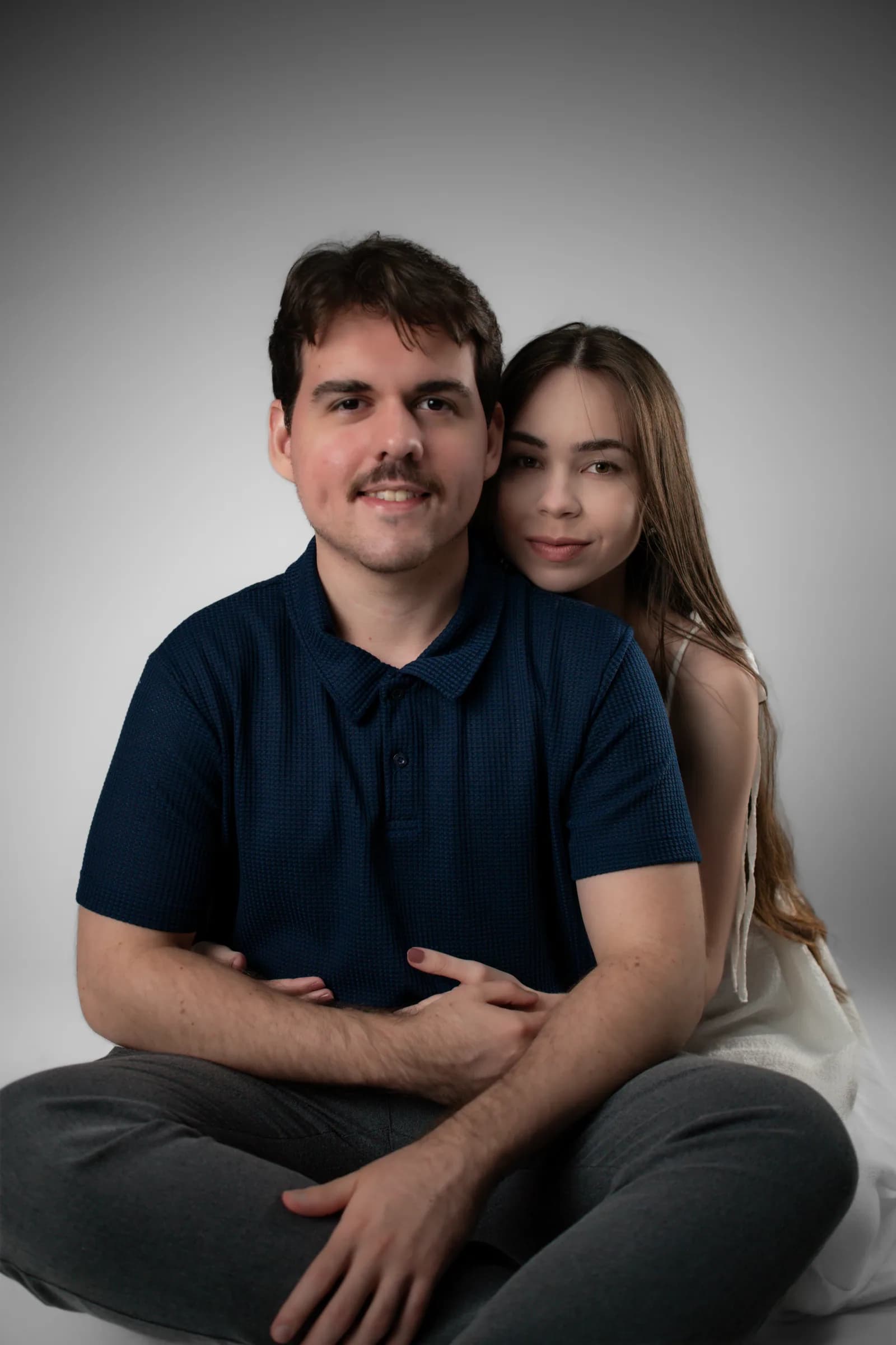 Casal sentado no chão, ela abraçada às costas dele