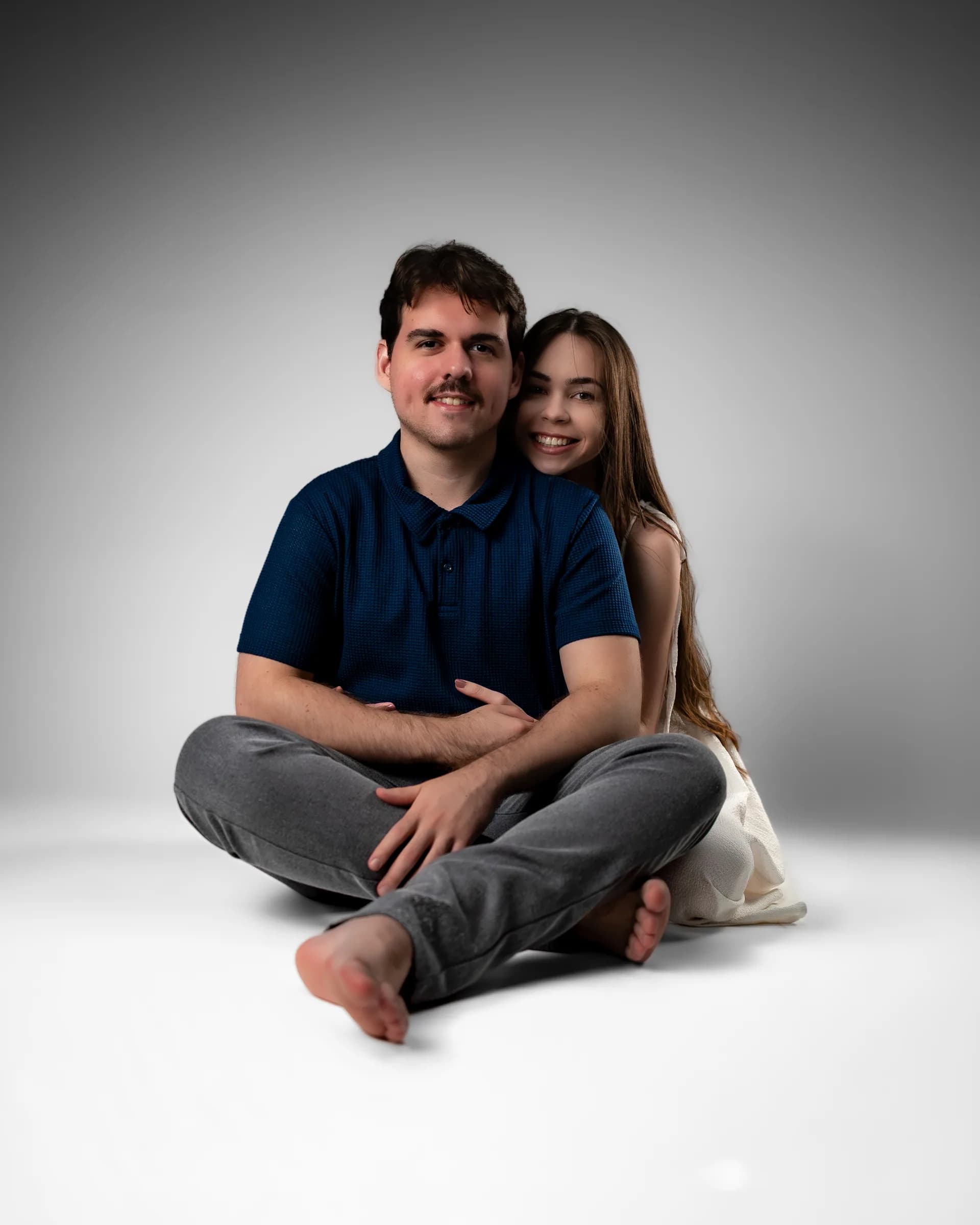 Casal sentado no chão de pernas cruzadas, sorrindo para a câmera
