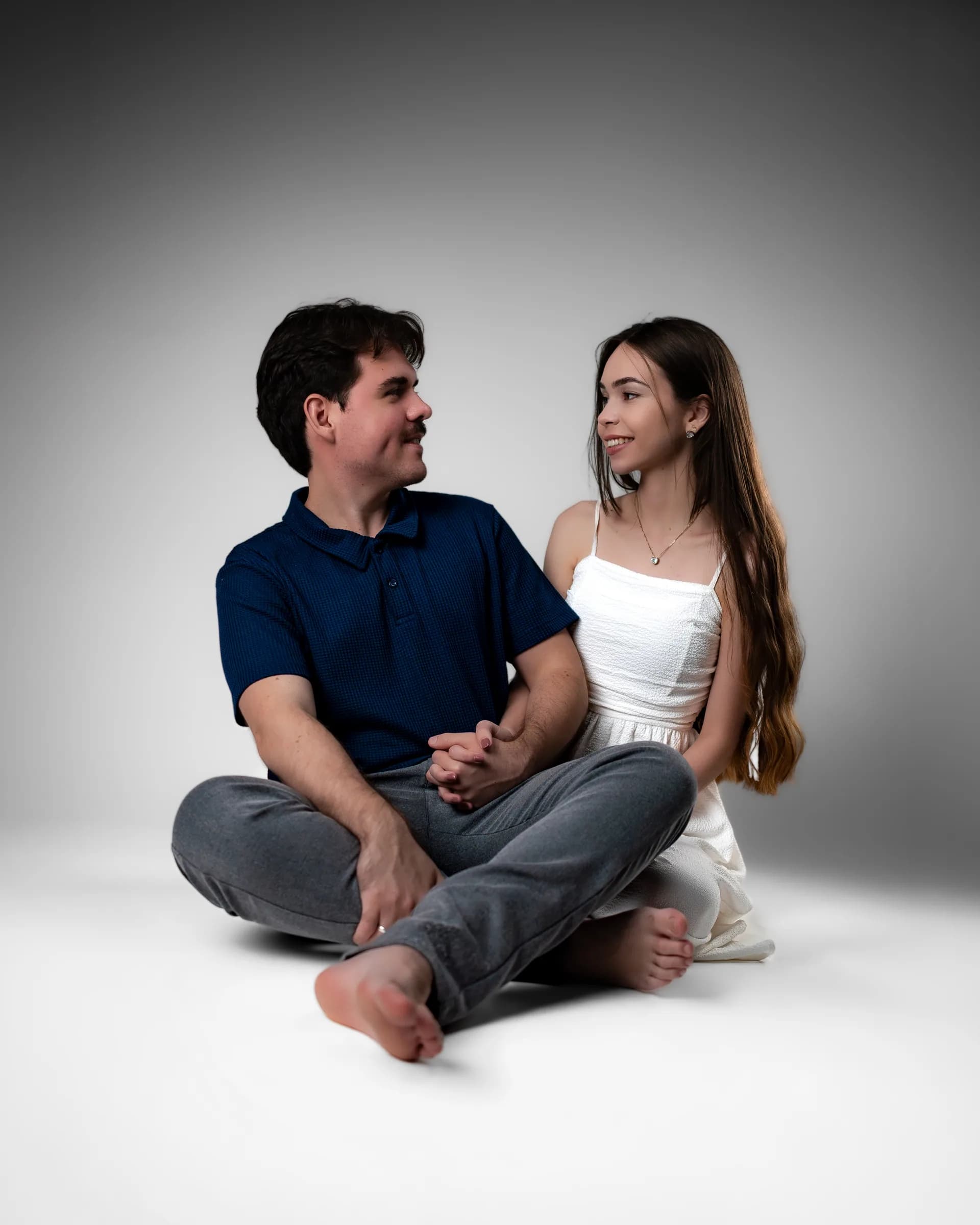 Casal sentado no chão, de mãos dadas, trocando olhares