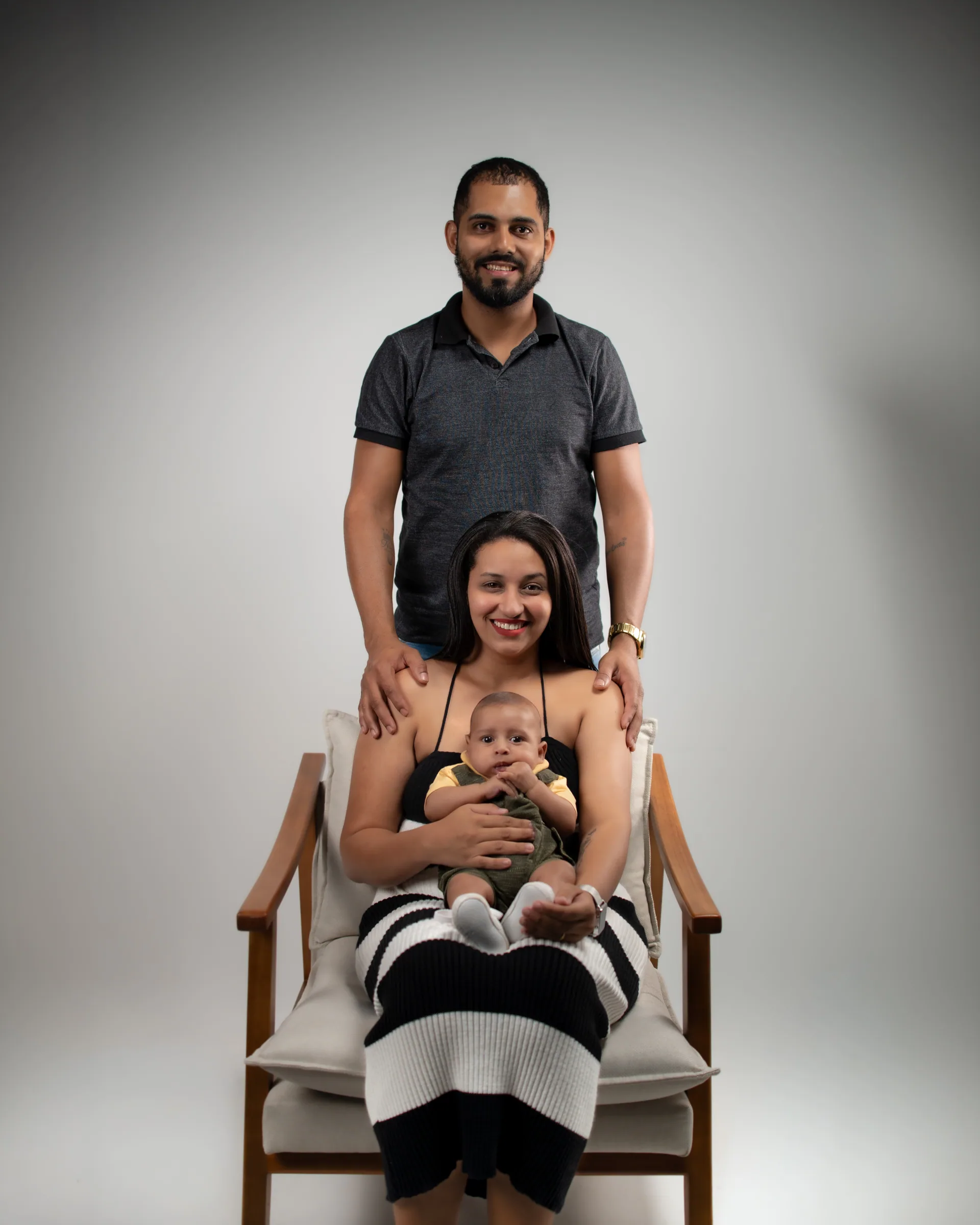 Mãe sentada na poltrona com o bebê no colo e o pai em pé atrás