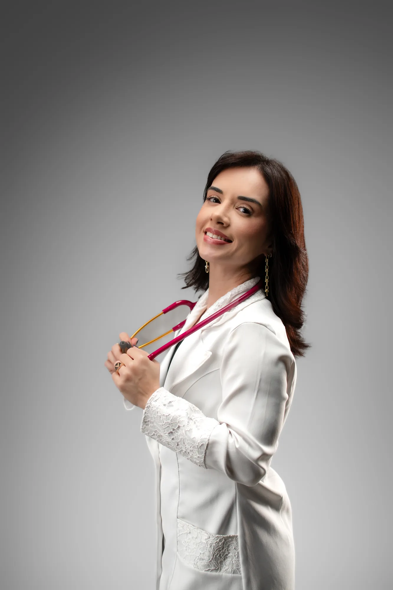 Médica de jaleco sentada numa poltrona de madeira, olhando para a câmera