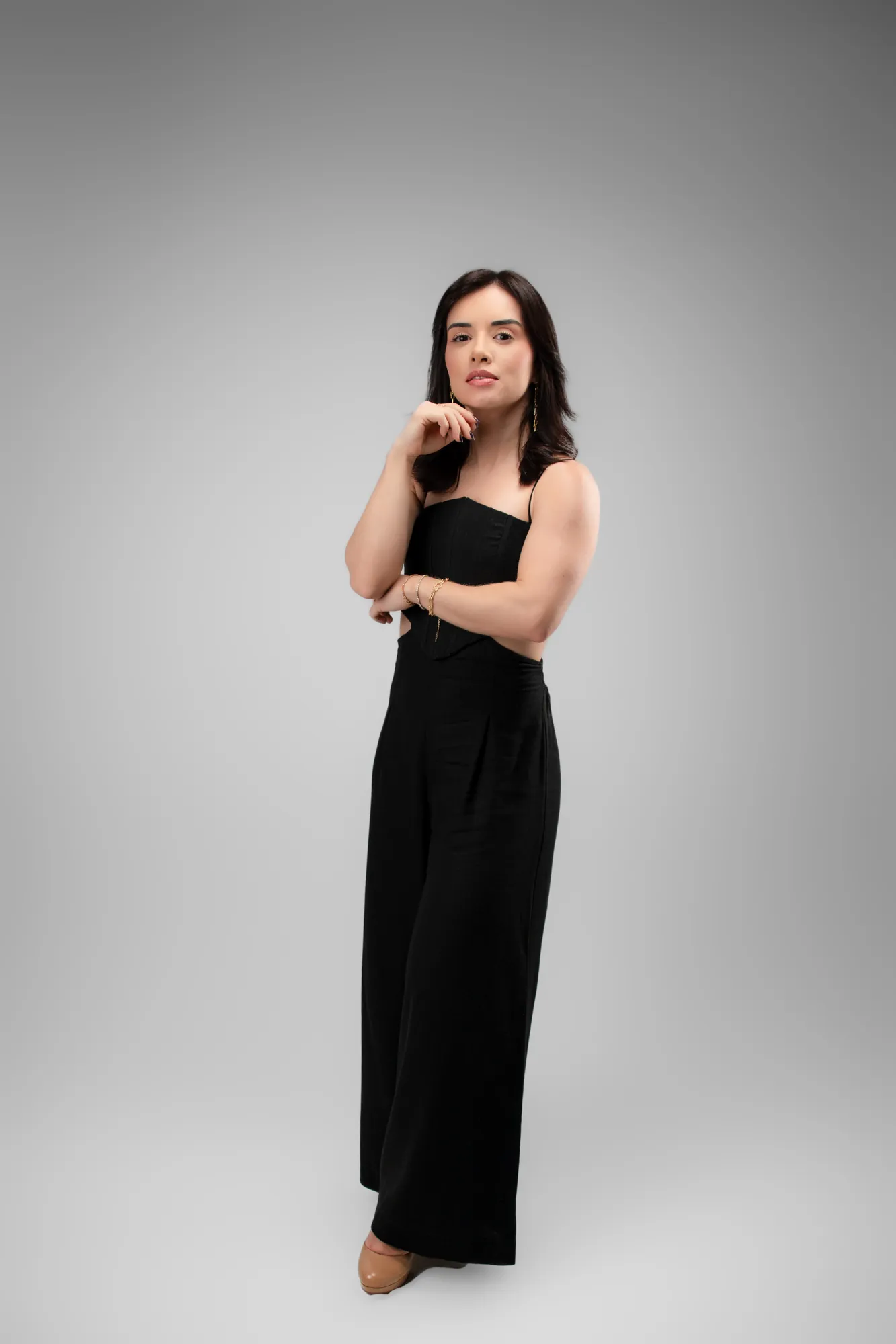 Mulher de vestido preto com a mão no queixo, olhando para a câmera