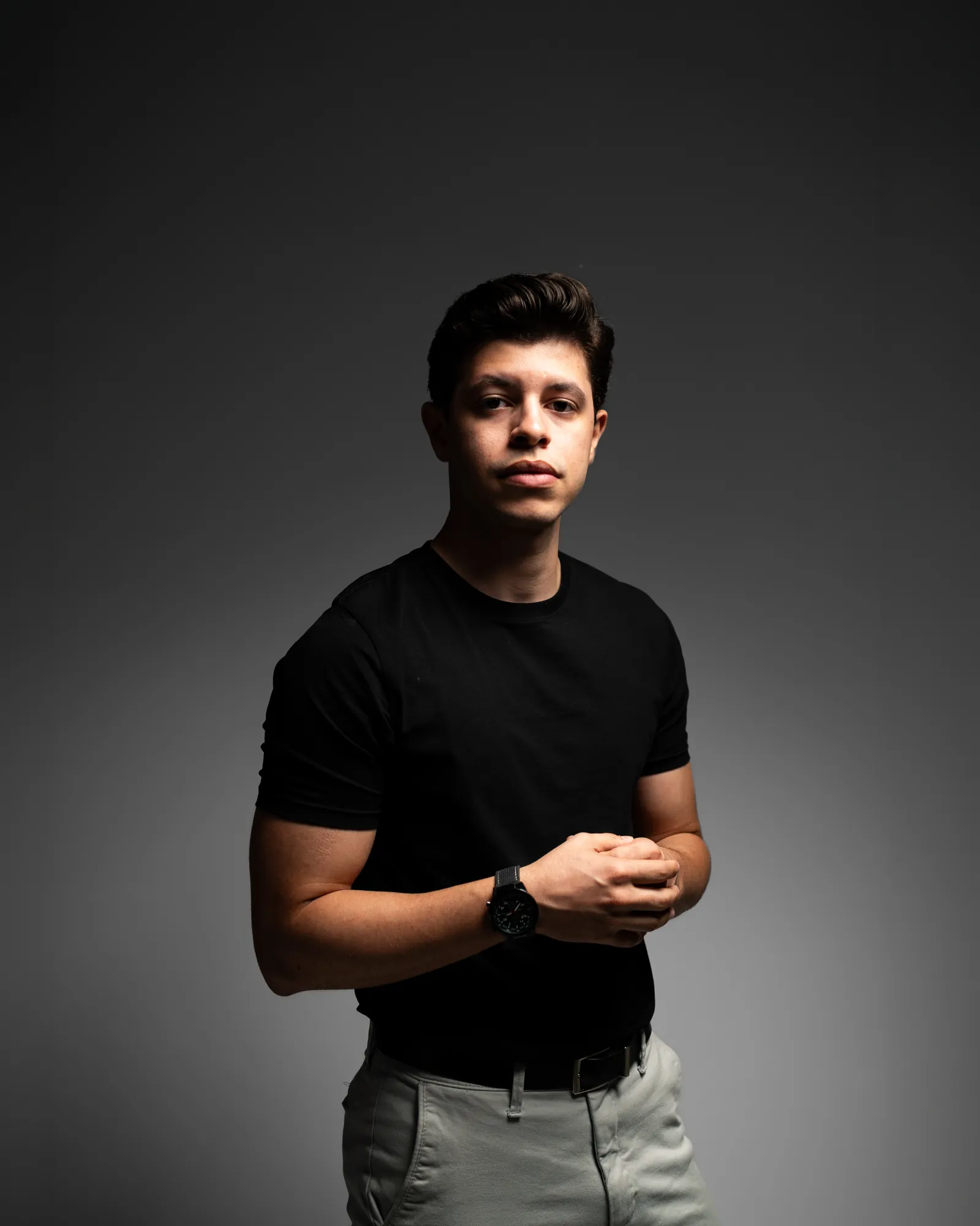 Jovem de camiseta preta sob luz dura, olhar sério, fundo escuro