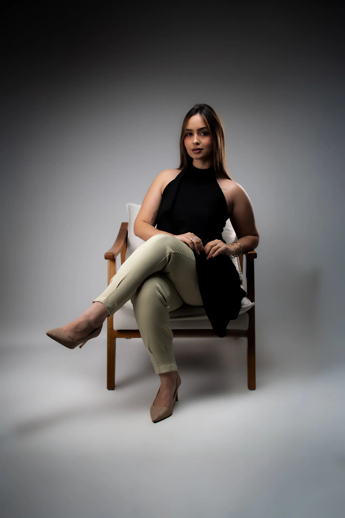 Mulher de calça clara e blusa preta sentada no chão, olhando para a câmera