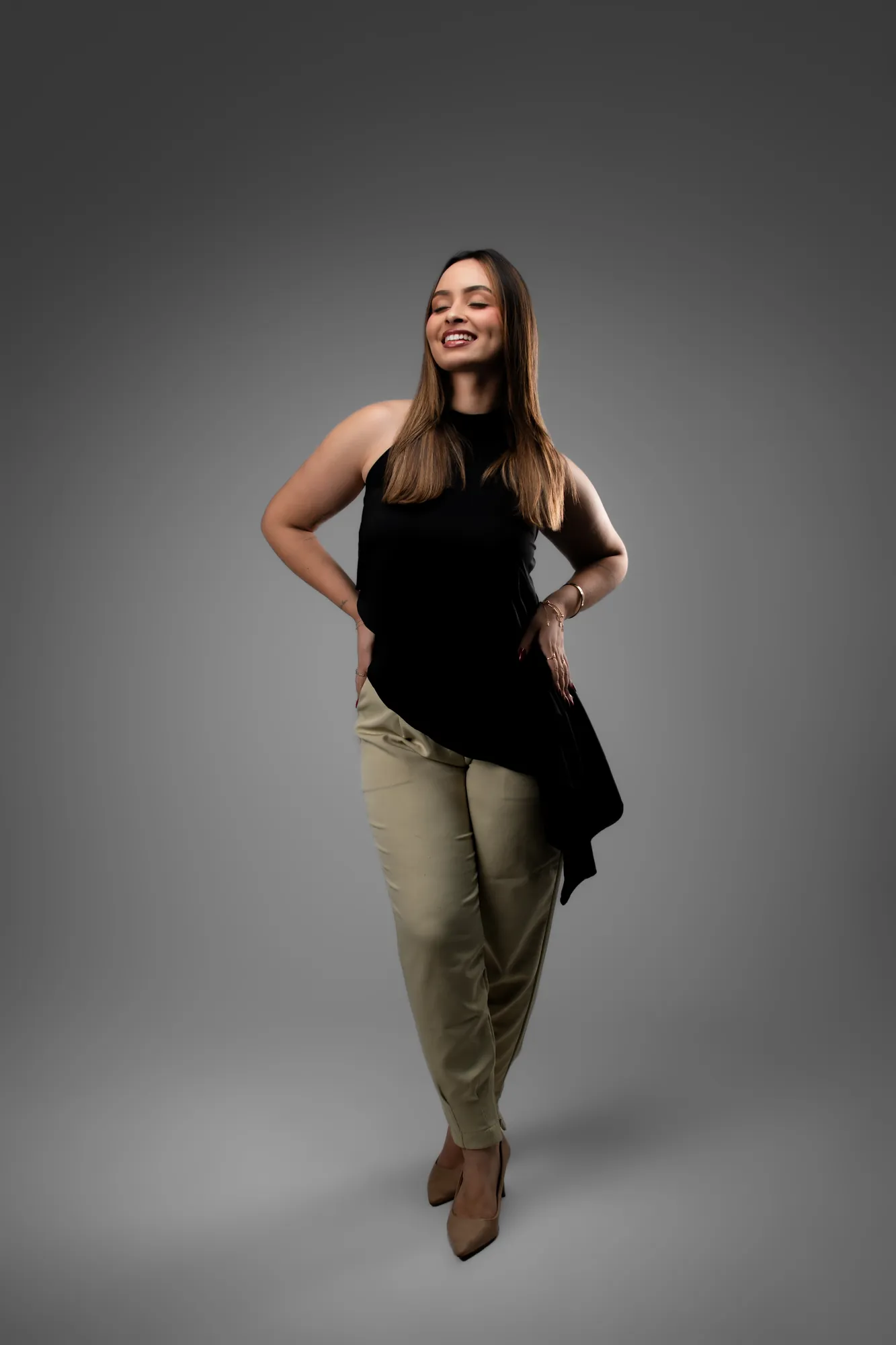 Mulher de blusa preta sorrindo de frente, as mãos à frente do corpo