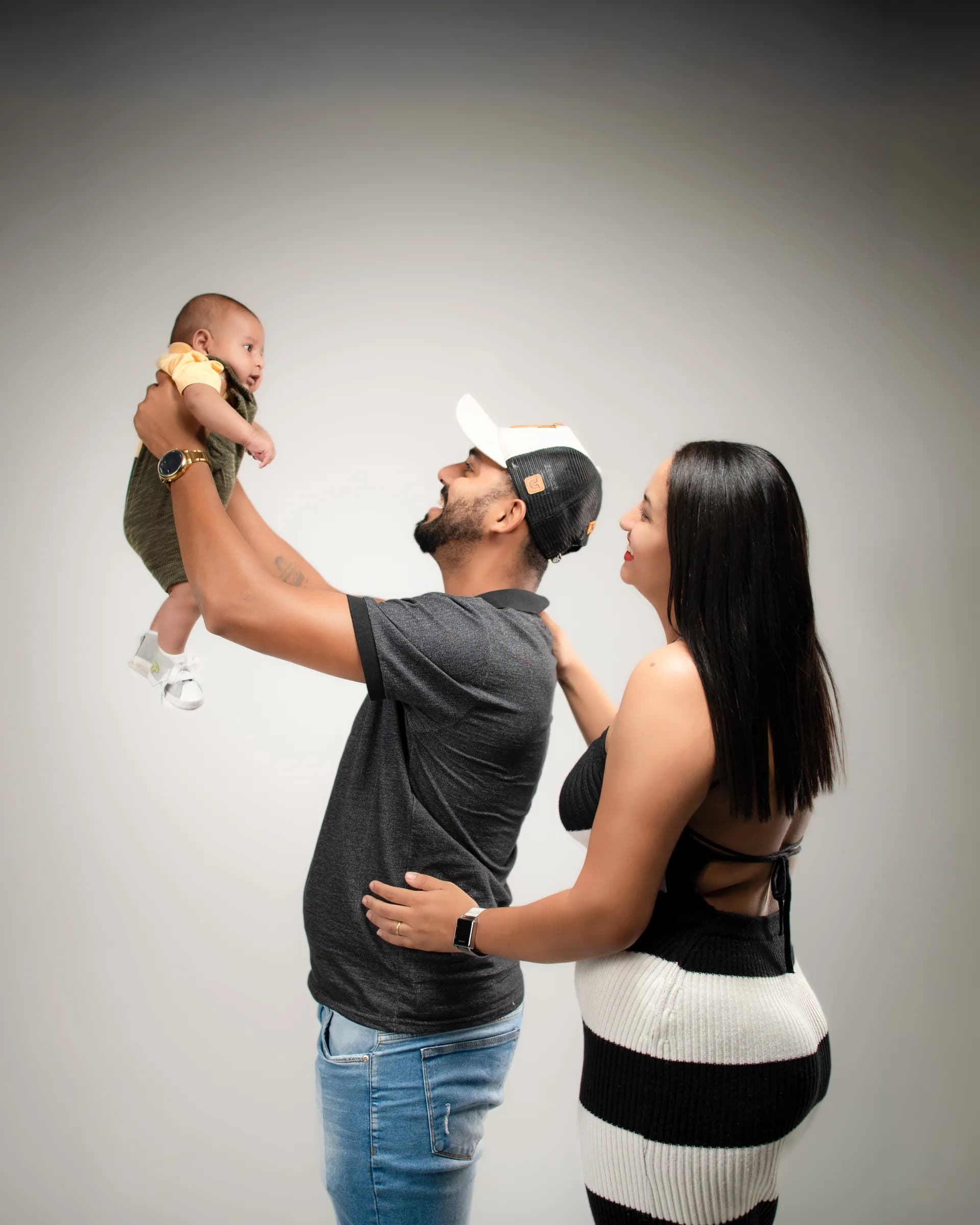 Pai levanta o bebê no alto enquanto a mãe acompanha o gesto